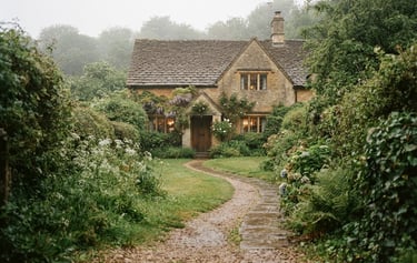 A misty gravel path leading to an old stone cottage in the Cotswolds, overcast sky, muted green foliage