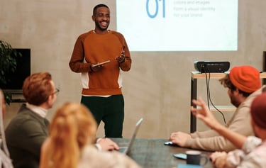 a man standing in front of a presentation on a projector to a group of people sitting and watching