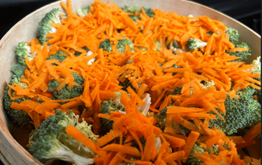 Broccoli florets and sliced carrots in a bamboo steamer ready to cook.