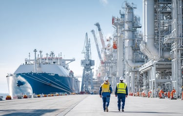two people in safety clothing walking toward a large energy carrier in an industrial setting