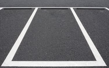 Straight-on eye-level shot of a clean, well-lit urban monthly parking lot in Tokyo, clear white line markings on dark asphalt, bright daylight with high visibility.