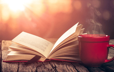 A book and cup of coffee on a table outside.