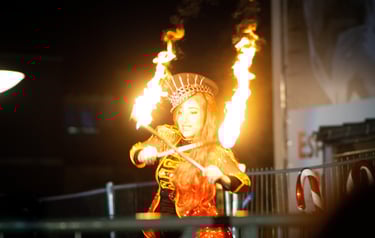 Une femme costumé en train de faire un spectacle avec des bâtons enflammés