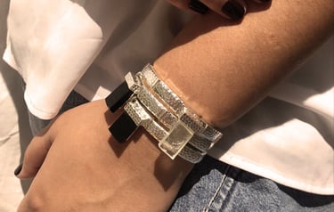 as mãos de uma mulher com um mix de pulseiras pratas com cristais e obsidiana negra