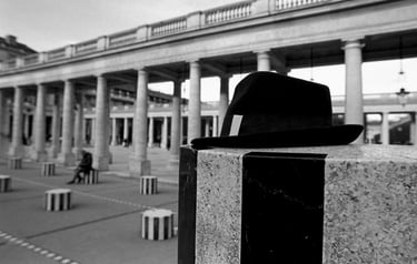 Black fedora hat resting on a stone pillar at the Palais-Royal in Paris, captured in black and white.