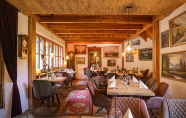 Rustikales Fine-Dining-Restaurant mit Holzbalken, Kunstwerken und eleganter Tischgestaltung.