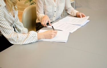 Two business women reviewing paper documents and taking notes during a professional office meeting.