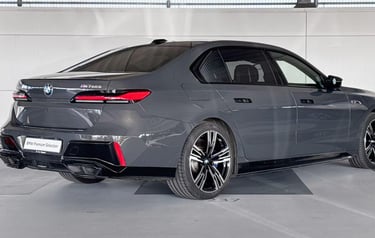 Rear view of a dark grey BMW M760e luxury plug-in hybrid sedan in a showroom.