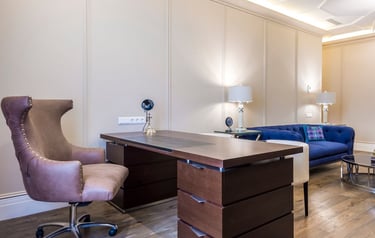 Modern home office featuring a dark wood executive desk, leather wingback chair, and blue velvet sofa.