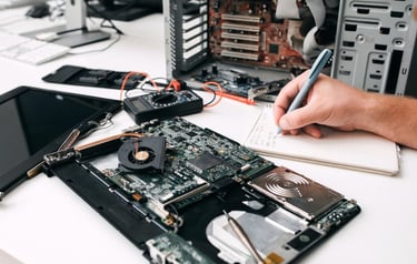 A technician repairing a laptop motherboard and taking notes for hardware diagnostics and computer maintenance.