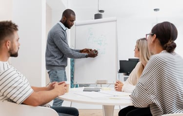 Un homme présente à un groupe lors d'une réunion devant un tableau blanc.
