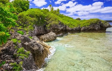 Tropical rocky coastline with stone steps leading into clear turquoise ocean water under a blue sky.