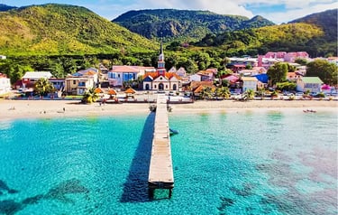 Aerial view of Anse d'Arlet beach in Martinique featuring a wooden pier, turquoise water, and a historic church.