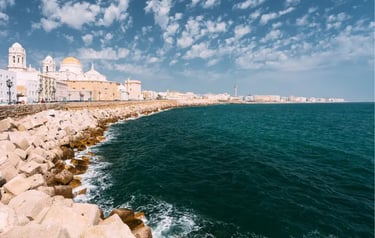 Panoramic view of the Cadiz Cathedral and rocky coastline against the blue Atlantic Ocean in Spain.