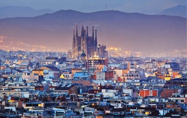 Barcelona city skyline at dusk featuring the Sagrada Familia basilica and misty mountains.