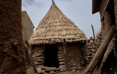 Traditional African mud hut with a conical thatched straw roof and stone entrance in a rural village.
