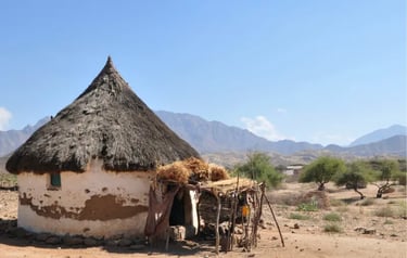 Traditional African round mud hut with a thatched roof in a dry mountain landscape.