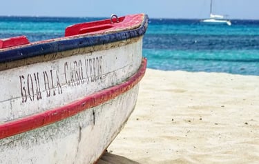 Rustic wooden fishing boat on a sandy beach in Cape Verde with turquoise ocean water in the background.