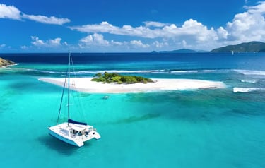 White sailing catamaran anchored in turquoise tropical waters near a sandy island cay under a blue sky.