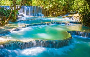 Kuang Si Falls features turquoise tiered pools and cascading waterfalls in a lush tropical jungle.