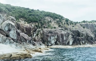 A white religious statue stands on a rocky cliffside along a rugged coastline by the sea.