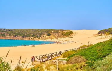 Panoramic view of Bolonia Beach in Tarifa, Spain, featuring sand dunes, turquoise ocean water, and a wooden walkway.