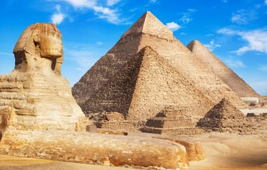 The Great Sphinx of Giza sitting in front of the ancient Egyptian pyramids under a clear blue sky.