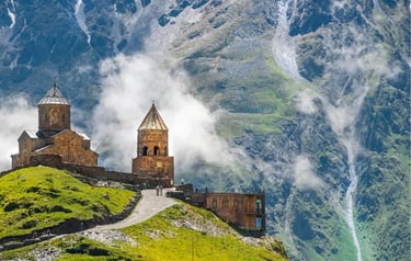 Gergeti Trinity Church stands on a lush green hill against the misty Caucasus Mountains in Georgia.