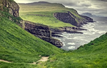 Scenic view of green grassy cliffs and rocky coastline overlooking the ocean in the Faroe Islands.