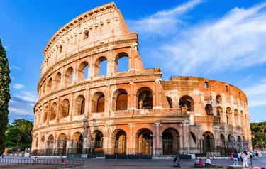 The Roman Colosseum in Italy, a historic stone amphitheater under a bright blue sky at sunset.