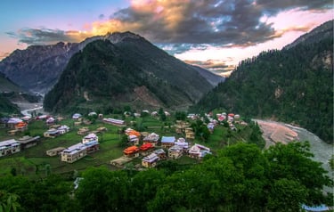Scenic mountain village nestled in a lush green valley with a river flowing under a sunset sky.