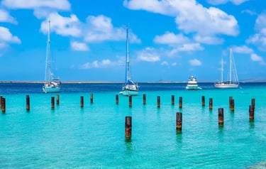 White sailboats anchored in tropical turquoise water with wooden pier pilings and a blue sky.