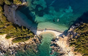 Aerial view of a secluded Greek island beach with crystal clear turquoise water and rocky coastline.