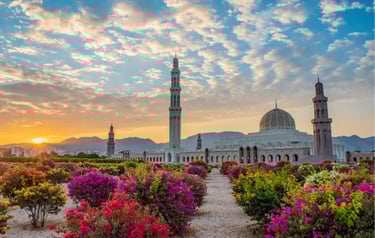Sultan Qaboos Grand Mosque in Muscat, Oman at sunset with colorful garden flowers in the foreground.