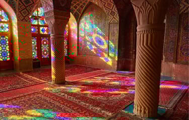 Stained glass light reflects colorful patterns on Persian rugs and carved pillars inside Nasir al-Mulk Mosque.