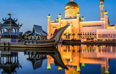 The Sultan Omar Ali Saifuddien Mosque in Brunei at dusk with a ceremonial stone boat reflected in the water.