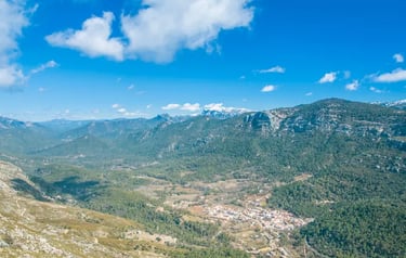 Panoramic view of a small mountain village nestled in a lush green valley under a bright blue sky.