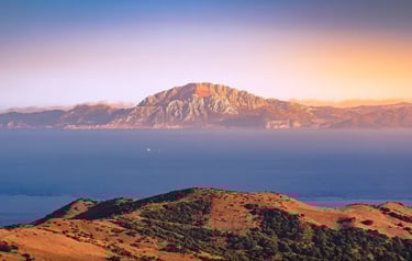 Scenic sunset view of the Rock of Gibraltar across the blue Mediterranean sea with coastal hills.