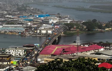 Aerial view of a busy bridge with heavy traffic crossing a river in a densely populated African city.