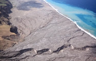 Aerial view of a volcanic landscape with black sand beach meeting turquoise ocean water.