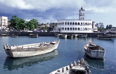 Traditional wooden dhow boats floating in the harbor of Moroni, Comoros, near a white domed mosque.