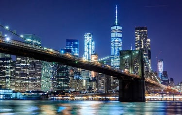 Brooklyn Bridge and Lower Manhattan skyline illuminated at night with One World Trade Center.