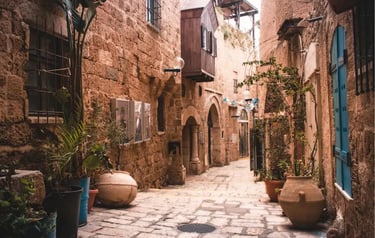 Narrow cobblestone alleyway in Old Jaffa with historic stone buildings and potted plants.