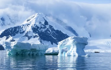 Blue icebergs floating in Antarctic waters with snow-covered mountains and an expedition boat.