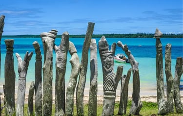 Traditional Kanak wooden totems carved with faces along a tropical turquoise beach in Vanuatu.