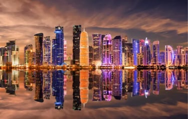 Night skyline of Doha, Qatar with illuminated skyscrapers reflected in the calm water of the bay.