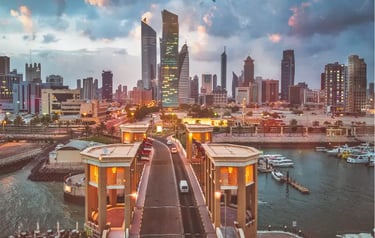 Panoramic sunset view of Kuwait City skyline with modern skyscrapers and the Sharq Marina waterfront.