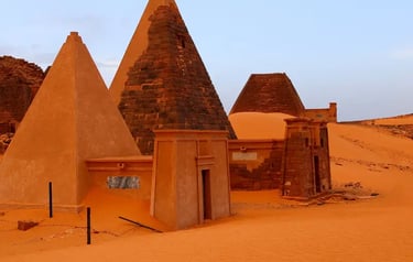 Ancient Nubian pyramids of Meroe in the Sudanese desert with orange sand dunes.