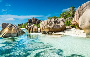 Pristine tropical beach with granite boulders, turquoise water, and palm trees in the Seychelles.