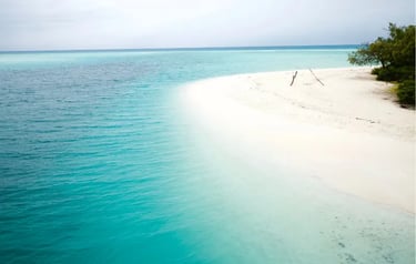Aerial view of a tropical white sand beach meeting turquoise ocean water under a cloudy sky.
